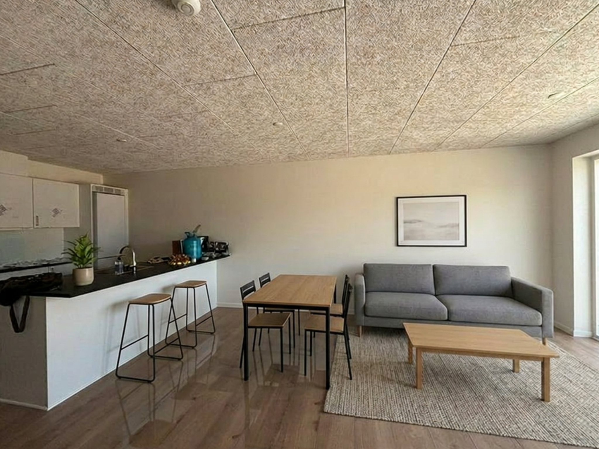Indretningsvisualisering af køkken-alrum med hvid køkkenhalvø, spisebord og grå sofa.