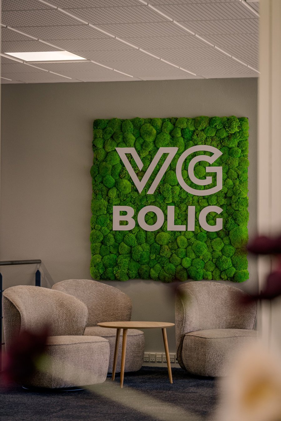 VG Boligs logo på en grøn mosvæg bag en siddegruppe